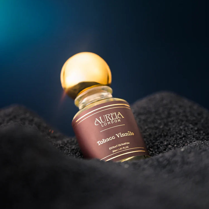 Aurelia London Tobacco Vainilo perfume bottle on a dark textured surface with a blue gradient background