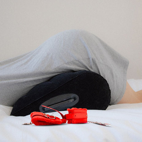 Person lying on a bed with a red travel pillow and strap in the foreground.