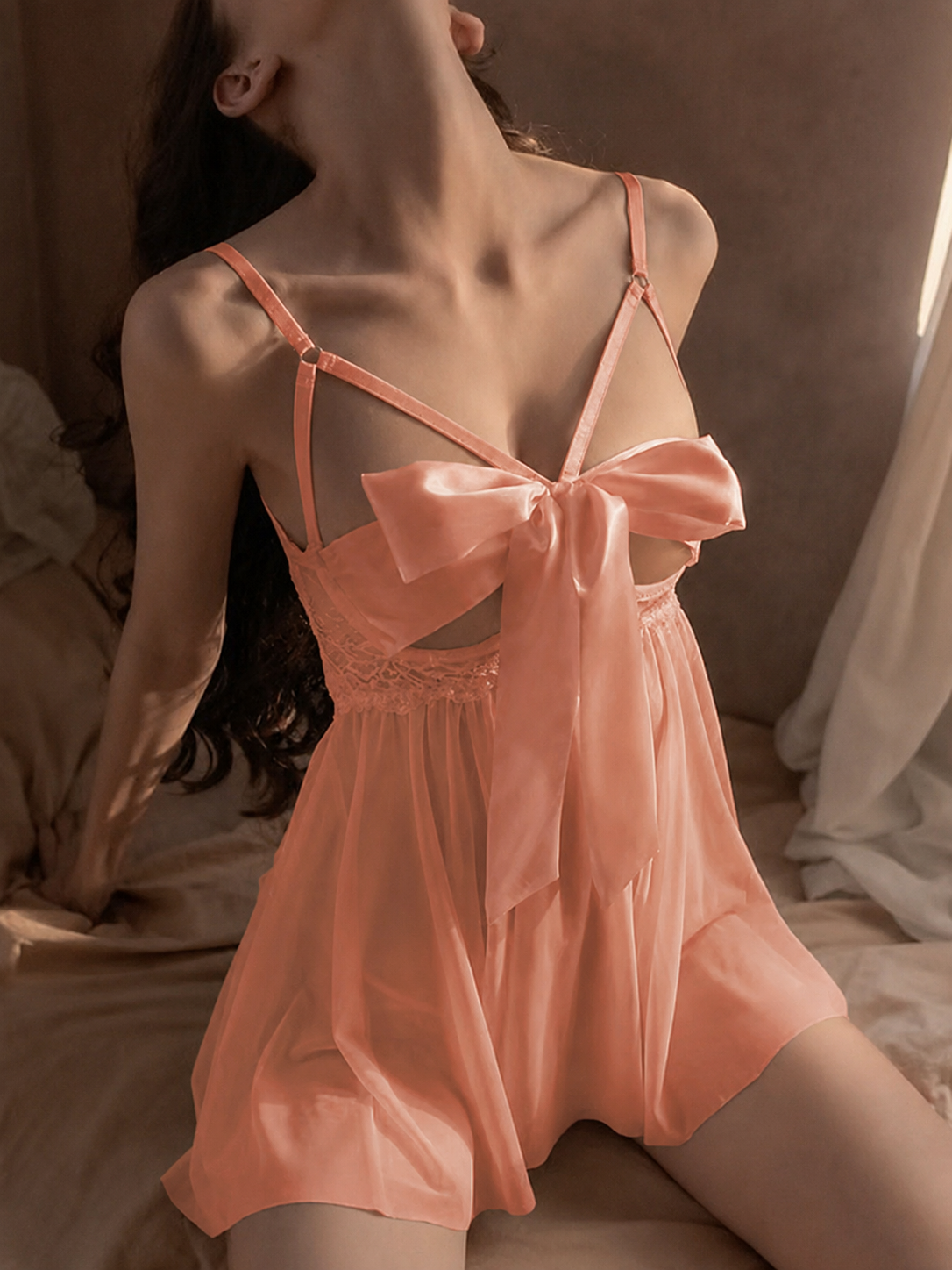 Woman wearing a pink nightgown with a bow detail in a softly lit room.
